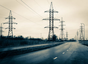 Electricity pylon on road against sky during winter