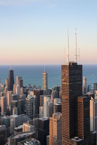 Modern buildings by sea against sky during sunset in city