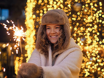 Portrait of woman standing against illuminated christmas tree