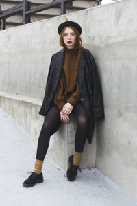 Portrait of young woman sitting on seat by wall