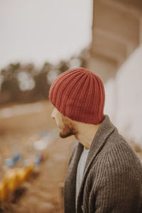 Side view of young man wearing knit hat standing against sky