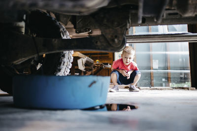 Boy looking at container below vehicle