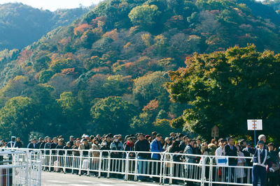 Crowd standing on street against tree mountains during autumn