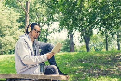 Mature man listening music while reading book in park