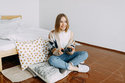 A girl in casual clothes plays on a video console sitting on the floor in the bedroom at home