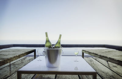 Glass of table by sea against clear sky