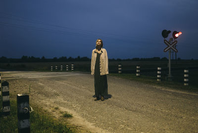 Woman standing near a railway crossing at night.