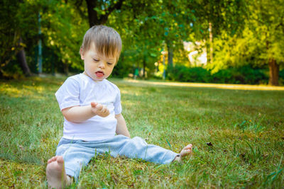 Cute boy sitting on grass against trees