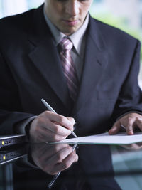 Midsection of businessman writing on document while sitting at desk