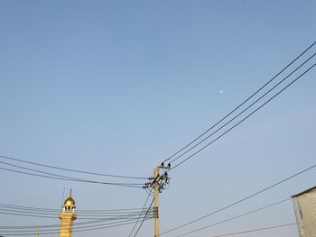 Low angle view of electricity pylon against clear blue sky