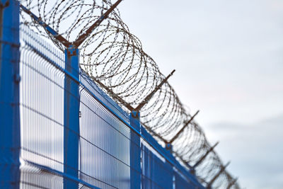 Low angle view of barbed wire on fence against sky