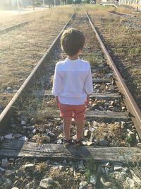 Rear view of boy standing on railroad tracks