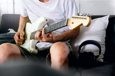 Man playing electrical guitar on sofa at home