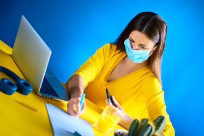Portrait of young woman using mobile phone while standing against blue background