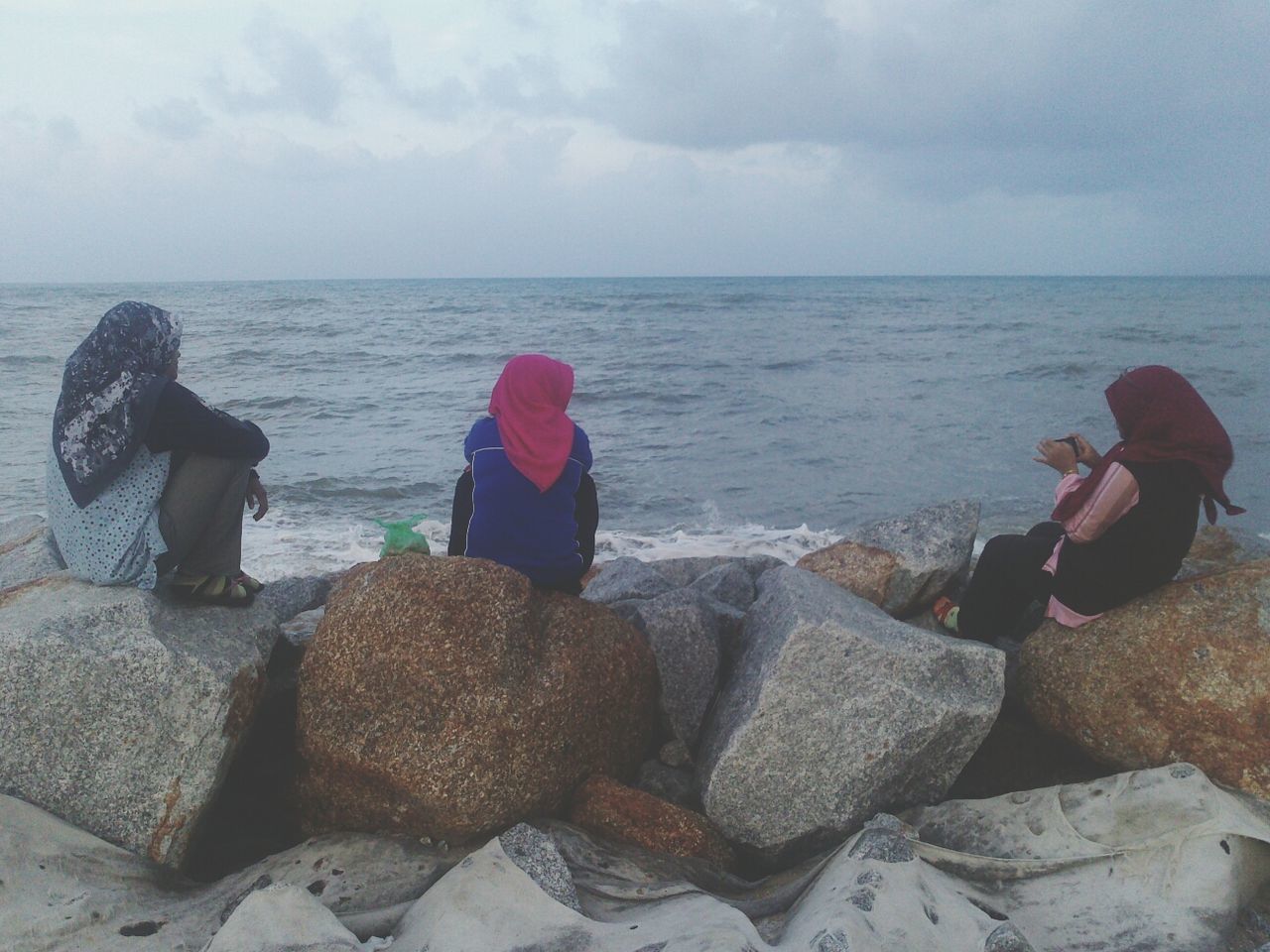 sea, water, sky, lifestyles, leisure activity, rock - object, horizon over water, sitting, cloud - sky, rear view, scenics, full length, casual clothing, standing, tranquility, beach, tranquil scene, relaxation