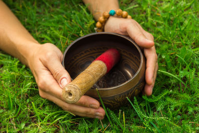 The hands of a young woman on tibetian singing bowl with wooden stick on the grass.
