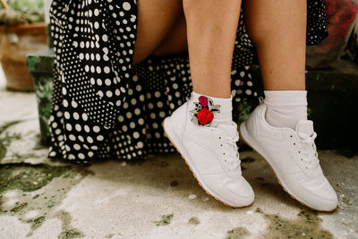 Low section of woman wearing white shoes on footpath