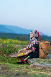 Woman sitting on field against sky