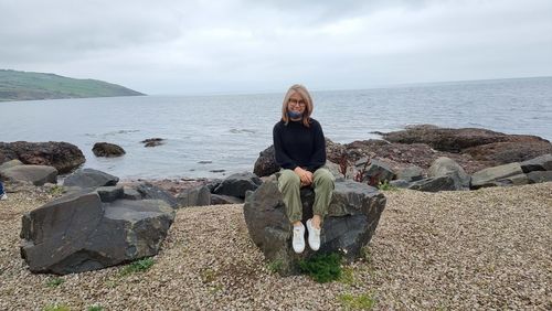 Rear view of woman sitting on rock by sea against sky