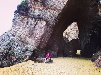 Rear view of woman sitting on rock by sea