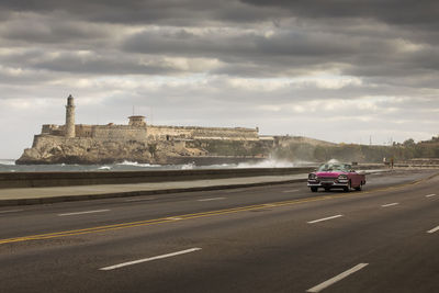 Cars on road against cloudy sky