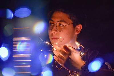 Portrait of man holding illuminated lighting equipment at night