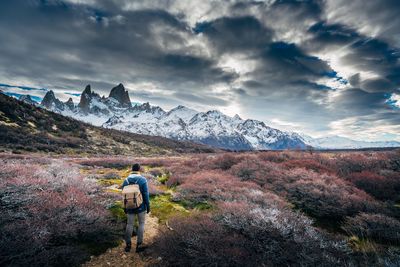 Rear view of man walking on mountain against cloudy sky