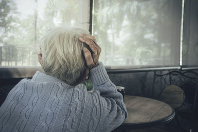 Rear view of old woman sitting by window at home. concept loneliness, dementia, abuse, sadness.