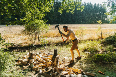 Full length of shirtless lumberjack cutting wood on field
