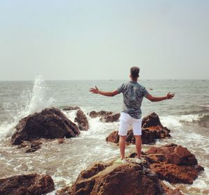 Rear view of woman standing on rock at beach