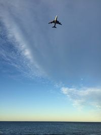 Low angle view of airplane flying over sea against sky