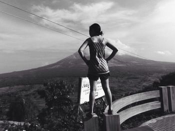 Woman standing on mountain against cloudy sky