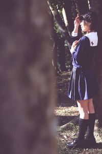 Woman wearing uniform standing by tree trunk at forest