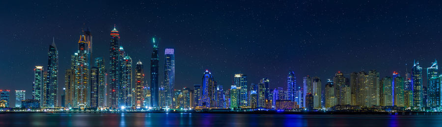 Illuminated cityscape by river against sky at night