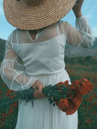 Midsection of woman holding flowers while standing by field