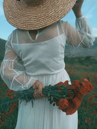 Midsection of woman holding flowers while standing by field