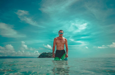 Portrait of shirtless man standing in sea against sky