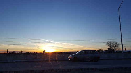 Cars on road against clear sky during sunset