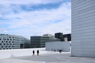 People walking by modern buildings in city against sky