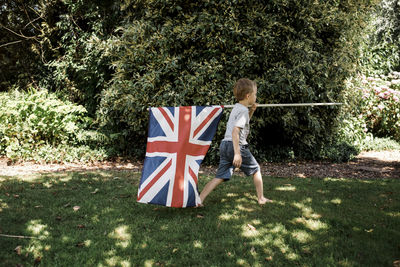 Side view of boy holding british flag while walking on grassy field at park