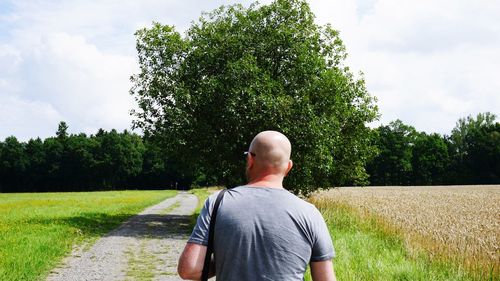 Rear view of bald man on field against sky during sunny day