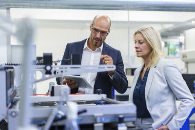 Confident businessman and businesswoman discussing while looking at machinery in factory