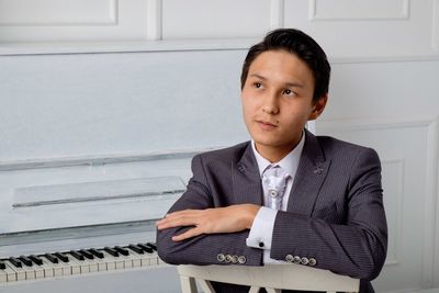 Thoughtful young businessman leaning by piano