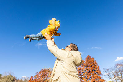 Low angle view of woman with arms raised standing against clear blue sky