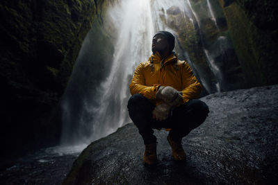 Full length of man crouching against waterfall in cave