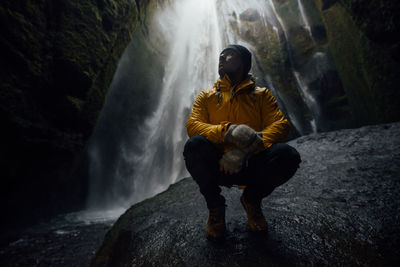 Rear view of woman standing on rock against waterfall