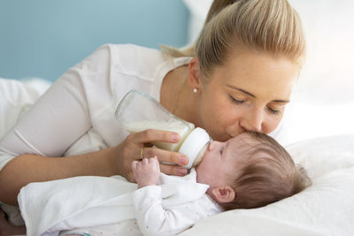 Mother feeding daughter on bed