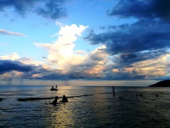 Silhouette people on sea against sky during sunset