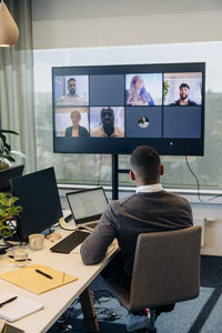 Rear view of businessman doing video conference with colleagues on tv screen in office