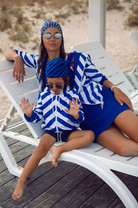 Mother and her baby son in striped blue jackets walk along the beach next to a wooden gazebo